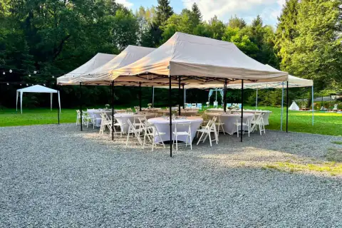 Tři party stany s kulatými stoly a bílými židlemi na štěrkové ploše
