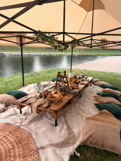 Piknik pod stanem u řeky s nízkým stolem a polštáři