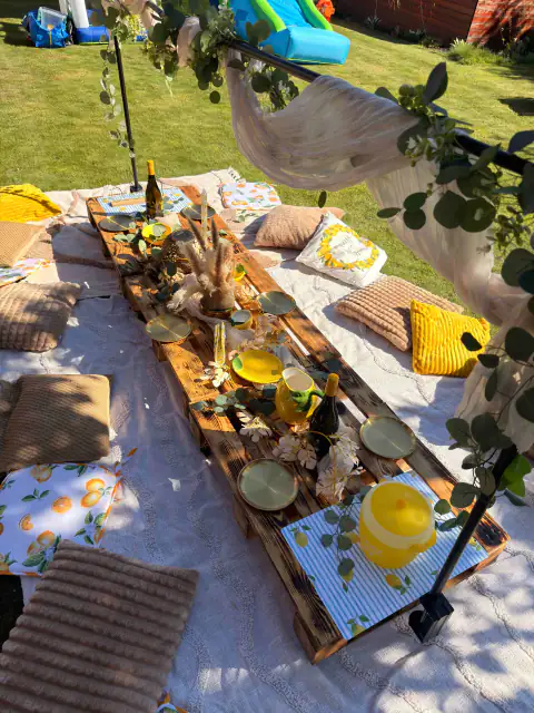 Piknik ve žlutých barvách s nízkým dřevěným stolem a polštáři