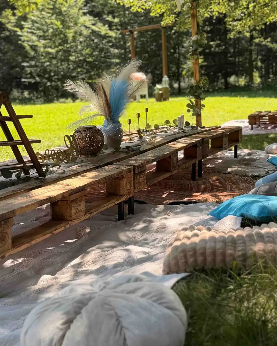 Boho piknik na zahradě s dlouhým nízkým stolem, polštáři a pampovou trávou